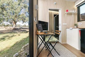 A room with a desk, chair, and a television. There is a window with a view of a tree and a building. - Cathedral Views by Tiny Away (Buxton)