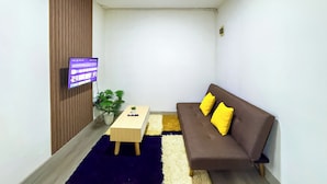Ein kleines, gut beleuchtetes Wohnzimmer mit Holzpaneelen, einem braunen Sofa mit gelben Kissen, einem kleinen Holztisch und einem Blumentopf.