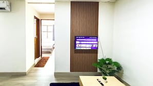 Ein modernes Wohnzimmer mit einem flachbildfernseher an einer Holzverkleidung, einem kleinen Tisch mit Fernbedienung und einem Blumentopf.