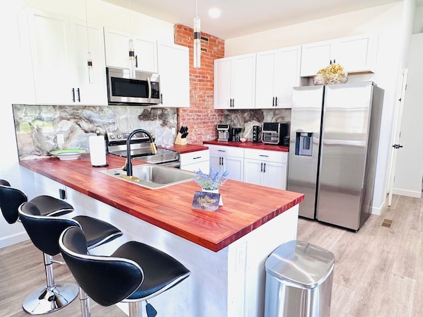 A modern kitchen with white cabinets, a wooden island with bar stools, stainless steel appliances, and a brick accent wall.