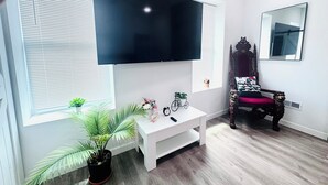 A modern living room with a large flat-screen TV mounted on the wall, a white entertainment unit, a vintage bicycle, and a classic wooden chair. - 4bed/3bath House in St. Louis (St. Louis)