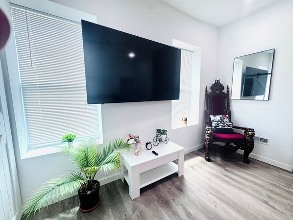 Una sala moderna con un televisor de pantalla plana grande montado en la pared, un mueble blanco para entretenimiento, una bicicleta antigua y una silla de madera clásica.