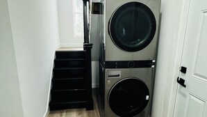 A laundry room with two stacked front-loading washing machines, a staircase, and a white door. - 4bed/3bath House in St. Louis (St. Louis)
