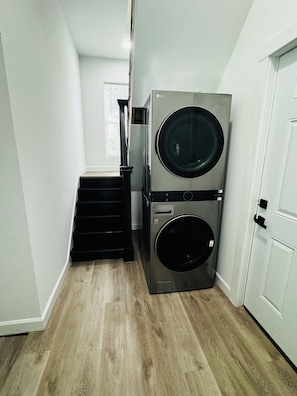 A laundry room with two stacked front-loading washing machines, a staircase, and a white door.