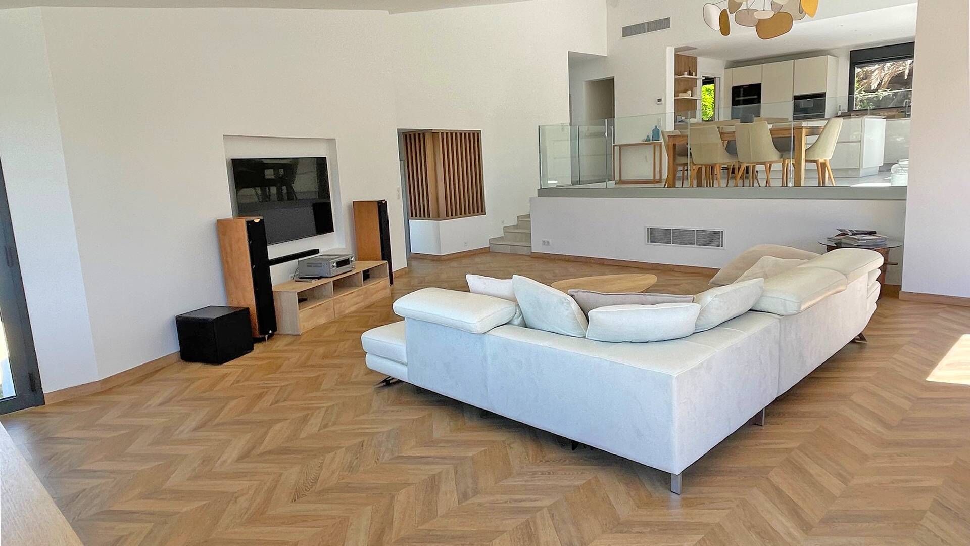 Een moderne woonkamer met een grote witte bank, een flatscreen televisie en een eethoek met een glazen tafel en stoelen.