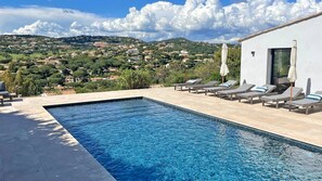A swimming pool with lounge chairs and a view of a hillside town. - Villa 6 rooms - 10 people (8 adults max) - Private pool - Air conditioning - WiFi - Sainte Maxime (STE MAXIME)