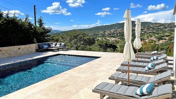 A swimming pool with lounge chairs and umbrellas, surrounded by a stone wall and overlooking a scenic hillside. - Villa 6 rooms - 10 people (8 adults max) - Private pool - Air conditioning - WiFi - Sainte Maxime (STE MAXIME)