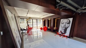 A modern hotel lobby with a polished floor, a reception desk, a large artwork, and a seating area with a red chair. - Apartamento Moderno en Ciudad Cayalá (Ciudad de Guatemala)