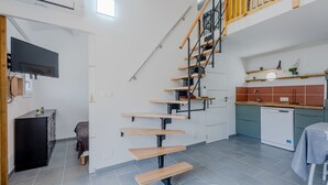 Un appartement moderne doté d’un escalier menant à une mezzanine, d’une cuisine équipée d’un lave-vaisselle et d’un téléviseur à écran plat fixé au mur.