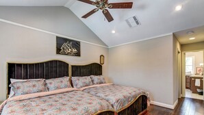 Un dormitorio con una cama, un ventilador de techo, un reloj de pared y un cuadro enmarcado.