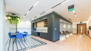 Una hall d'albergo moderna con un'area salotto centrale, un angolo cottura e un estintore appeso al muro.
