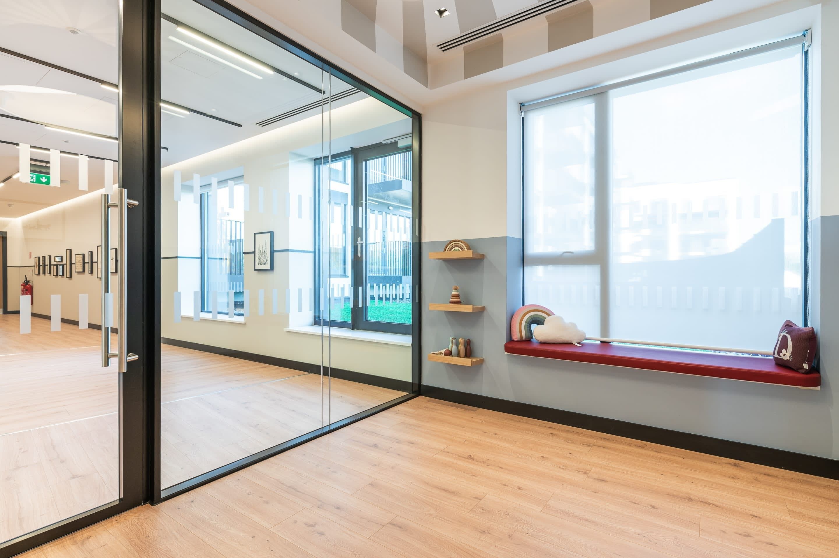 Un intérieur moderne avec des murs en verre, un plancher en bois, un banc rouge et une fenêtre offrant une vue dégagée.