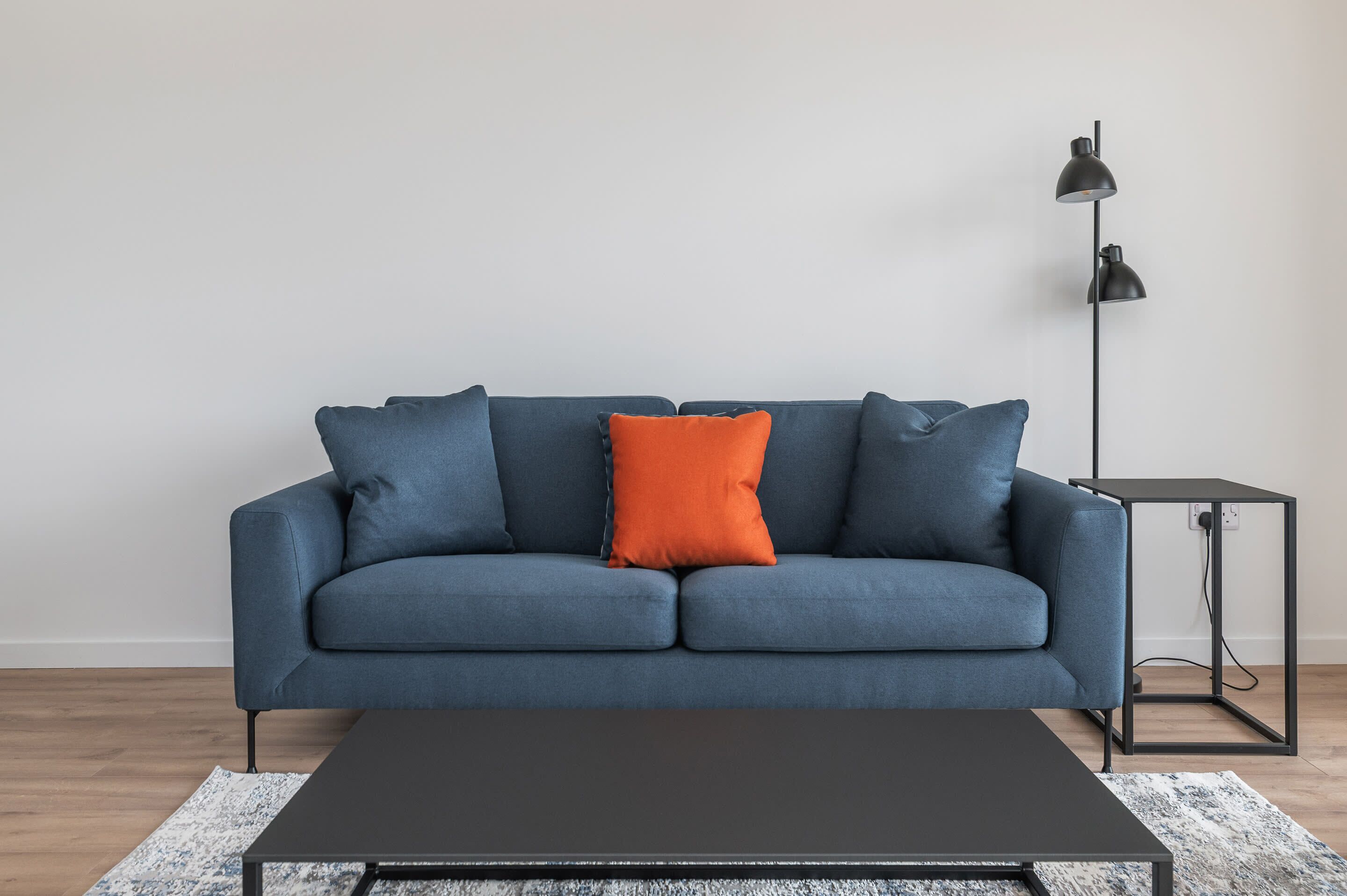 A blue sofa with an orange pillow, a black coffee table, and a floor lamp.