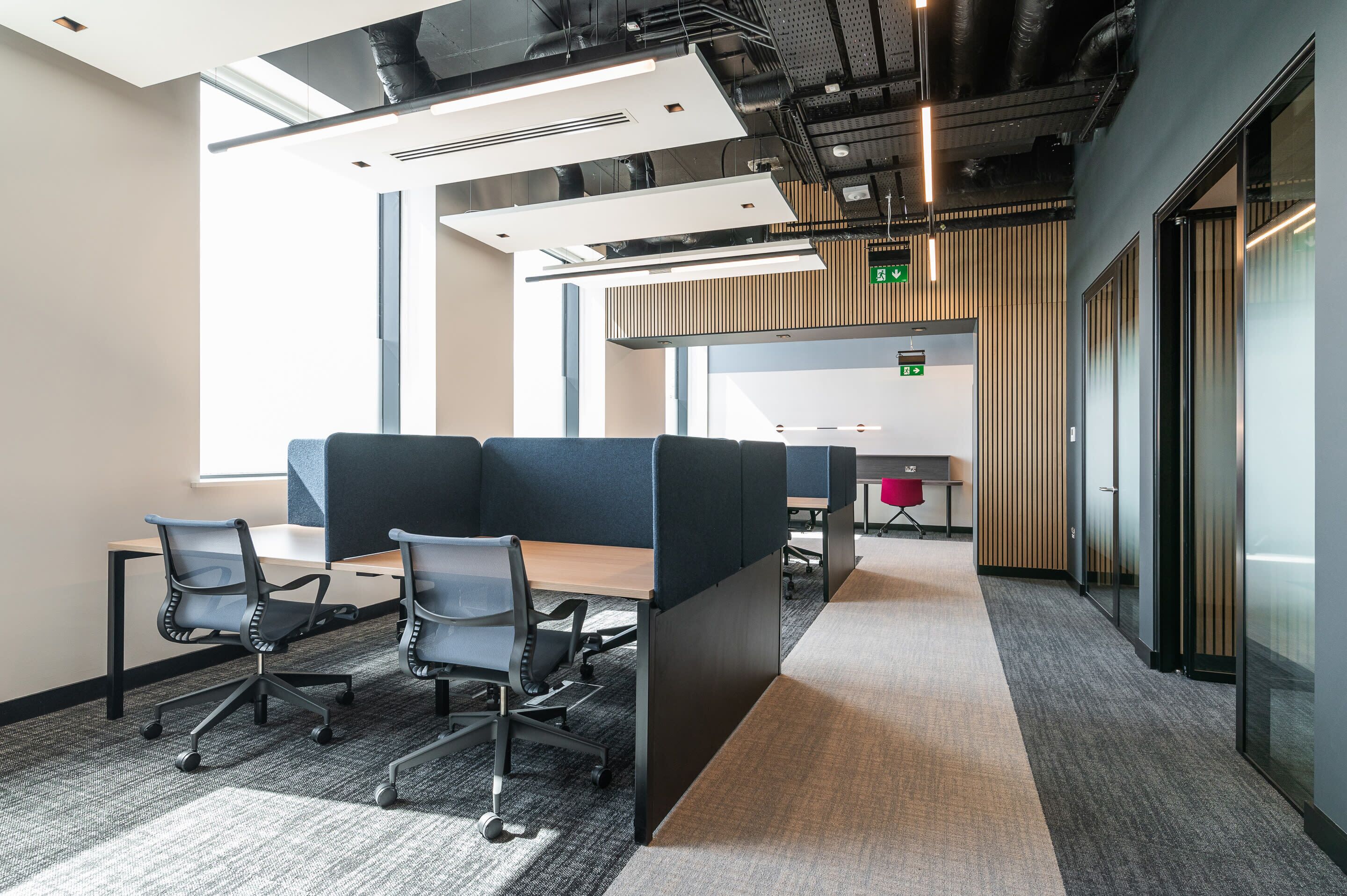A modern office space with cubicles, a meeting table, and a visible exit sign.