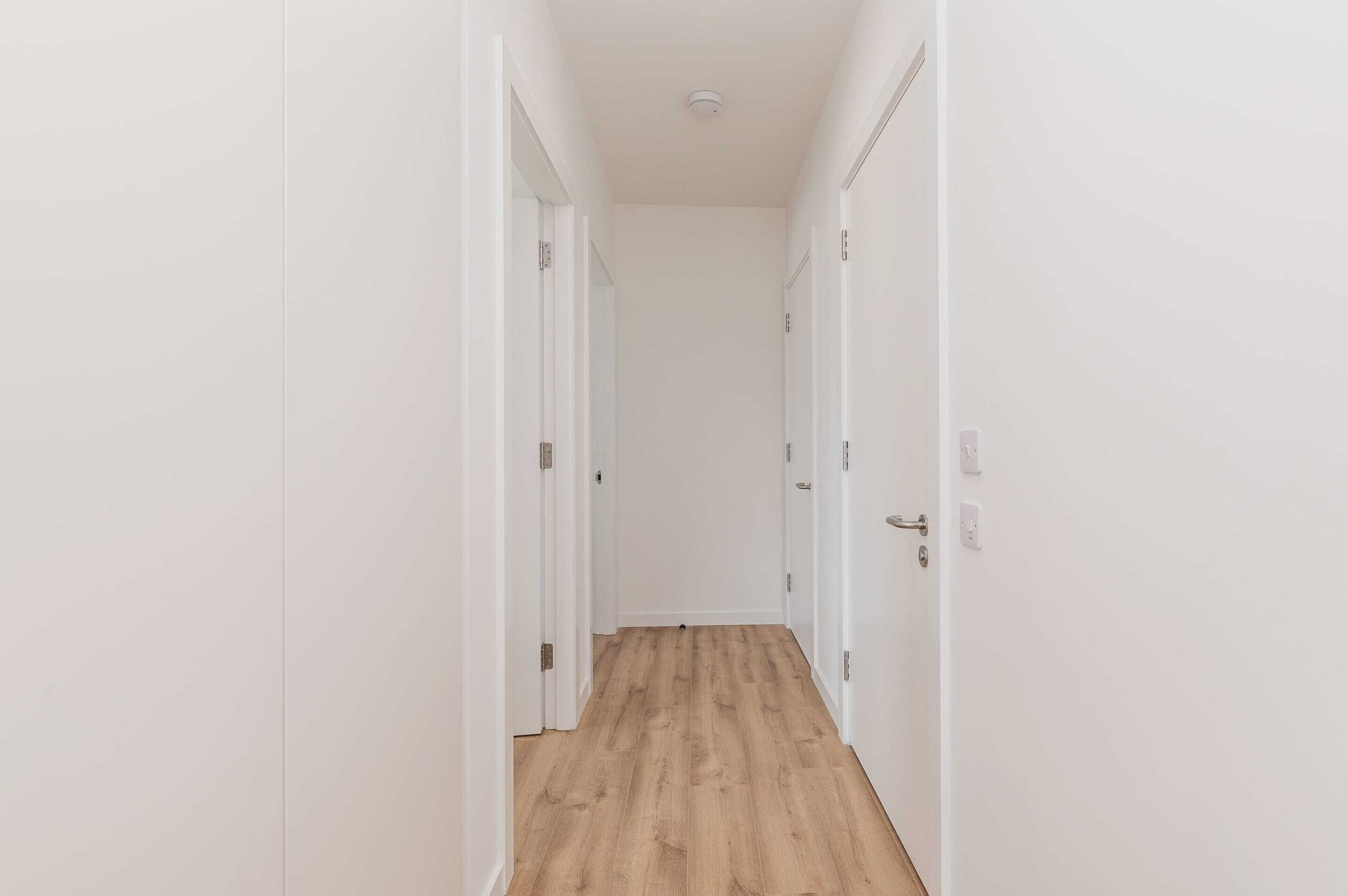 A narrow hallway with white walls and wooden flooring.