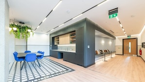 Un hall d’hôtel moderne avec un espace salon central, une kitchenette et un extincteur fixé au mur.