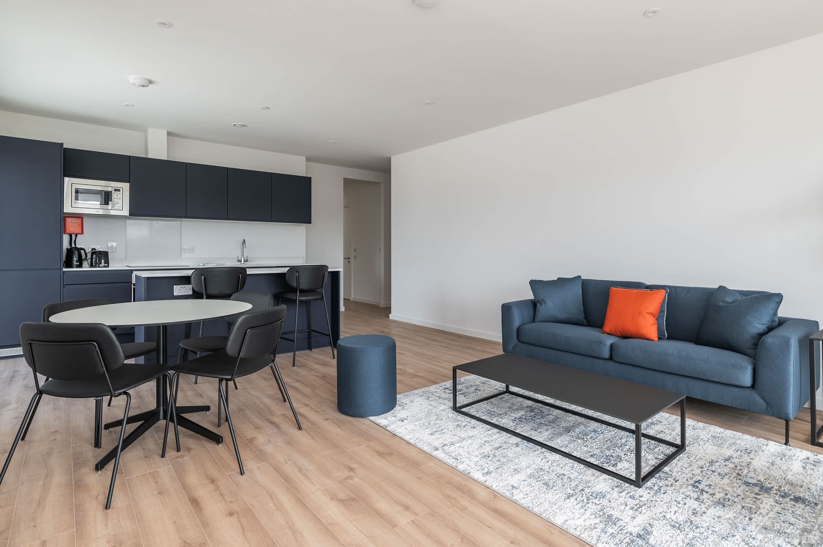 A modern living space with a dining area, a sofa, and a kitchen.