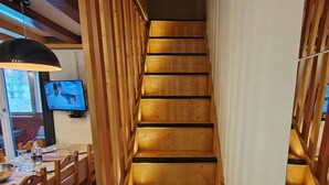 A wooden staircase with a modern design, leading to a dining area with wooden furniture and a television on the wall. - Friendly duplex 6 people. 39m² 3 separate sleeping areas, EAST balcony view. (VAL THORENS)