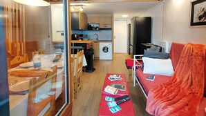A compact living space with a kitchenette, a dining area, and a seating area with a red sofa and ottoman. - Friendly duplex 6 people. 39m² 3 separate sleeping areas, EAST balcony view. (VAL THORENS)