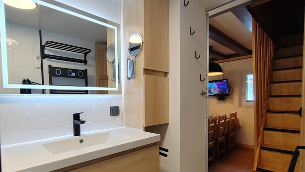 A modern bathroom with a white sink, wooden vanity, and a large mirror. A television is mounted on the wall, and there is a wooden staircase leading to another room. - Friendly duplex 6 people. 39m² 3 separate sleeping areas, EAST balcony view. (VAL THORENS)