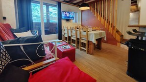 A cozy living room with a sofa, a dining table with chairs, a TV mounted on the wall, and a staircase with wooden railings. - Friendly duplex 6 people. 39m² 3 separate sleeping areas, EAST balcony view. (VAL THORENS)