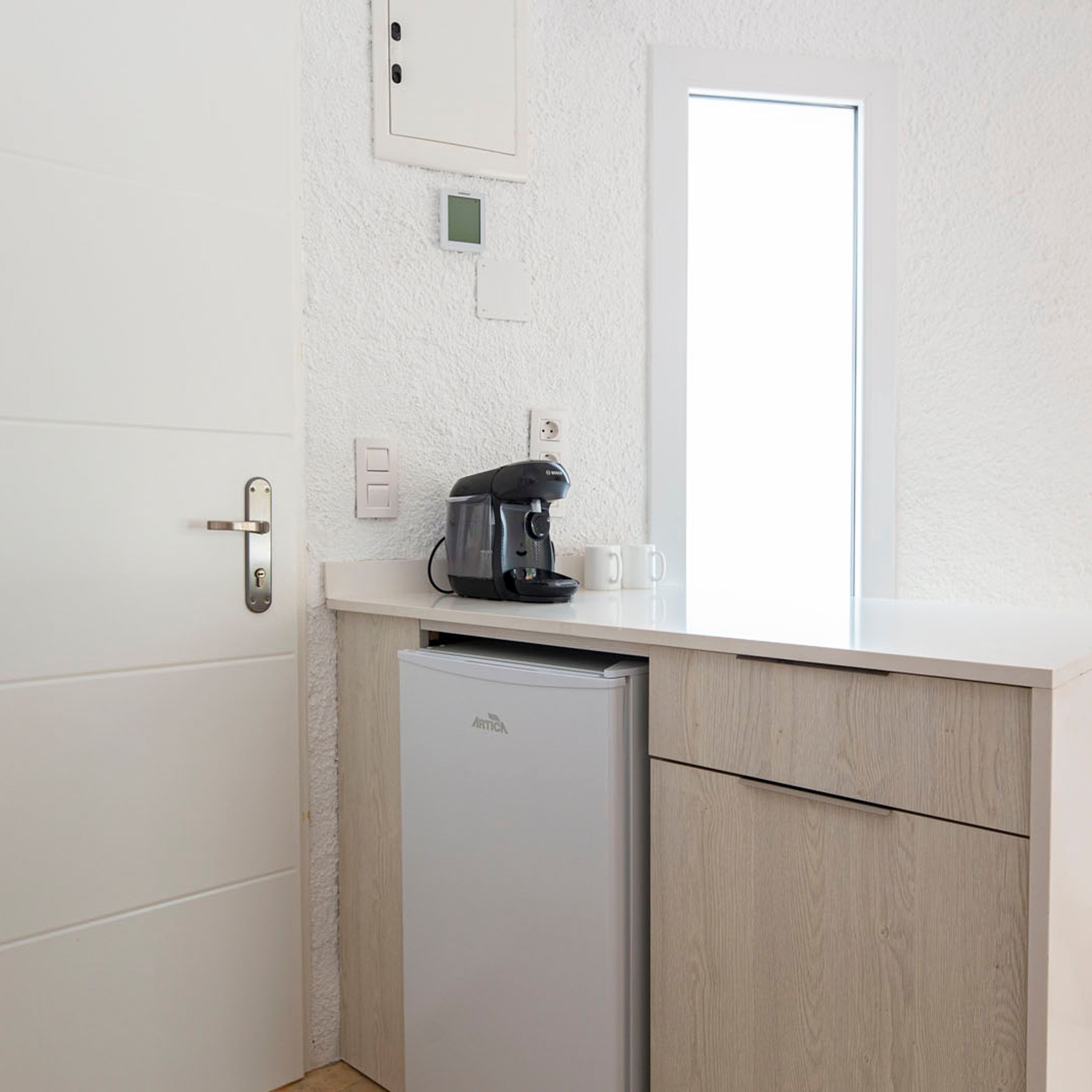 Een compacte kitchenette met een koffiezetapparaat, een kleine koelkast en een wit aanrecht.