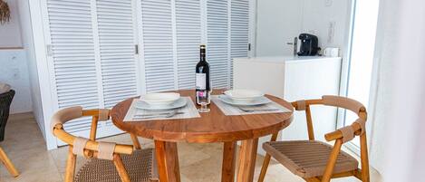 A dining area with a round wooden table, two wicker chairs, and a bottle of wine.