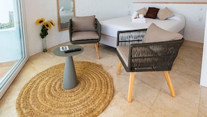 Una habitación moderna y luminosa con una cama, dos sillas, una mesita, un espejo y una lámpara colgante.