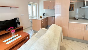 A modern kitchen with wooden cabinets, a built-in oven, and a sink. There is a dining area with a table and chairs, and a bed with a white cover. - Sant Sebastia 111 in Roses (Roses)