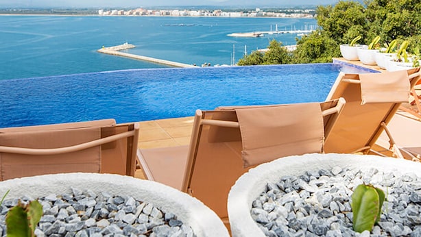 An infinity pool with a view of the sea and a distant cityscape.
