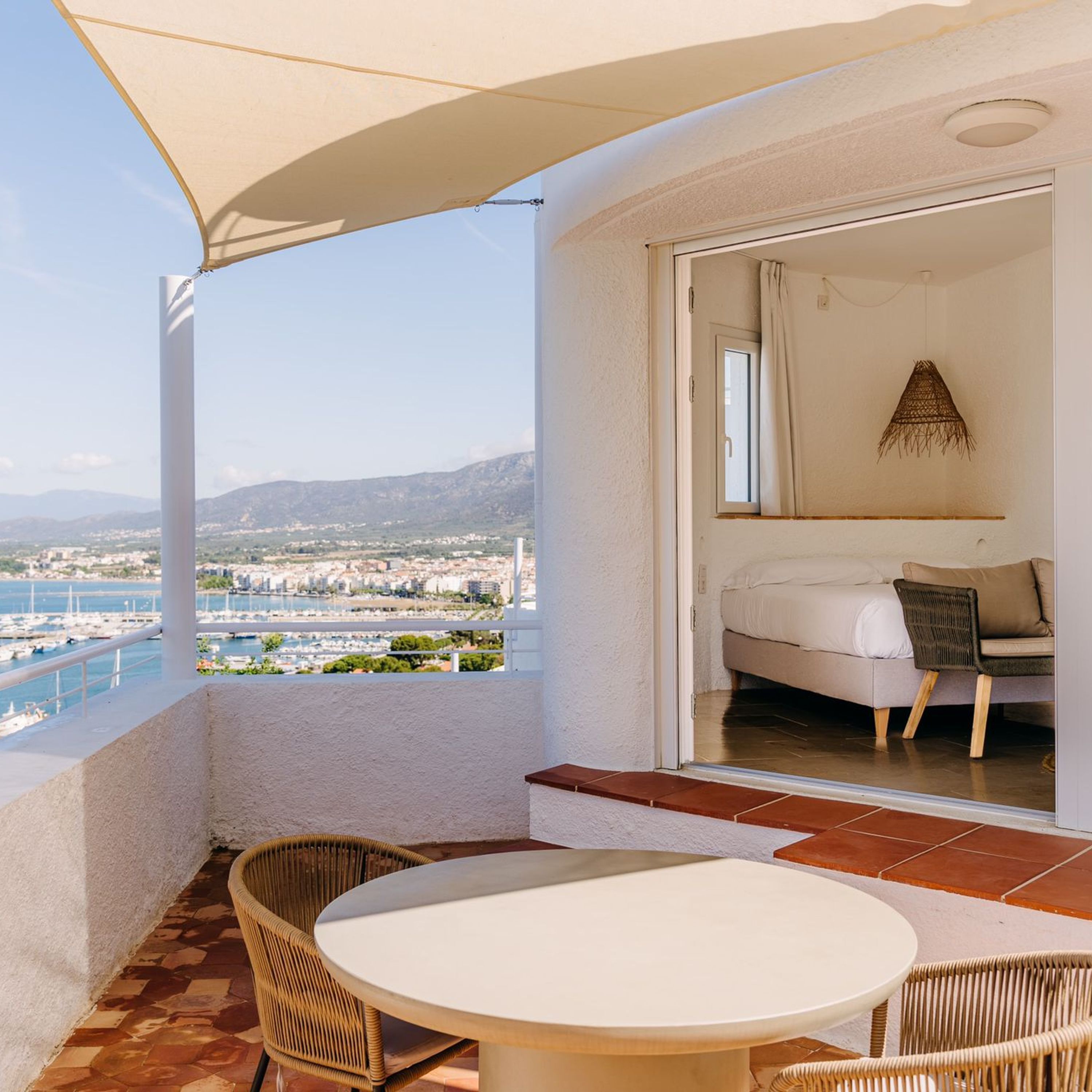 Un balcon avec une table et des chaises, un lit avec vue et un paysage urbain en arrière-plan.