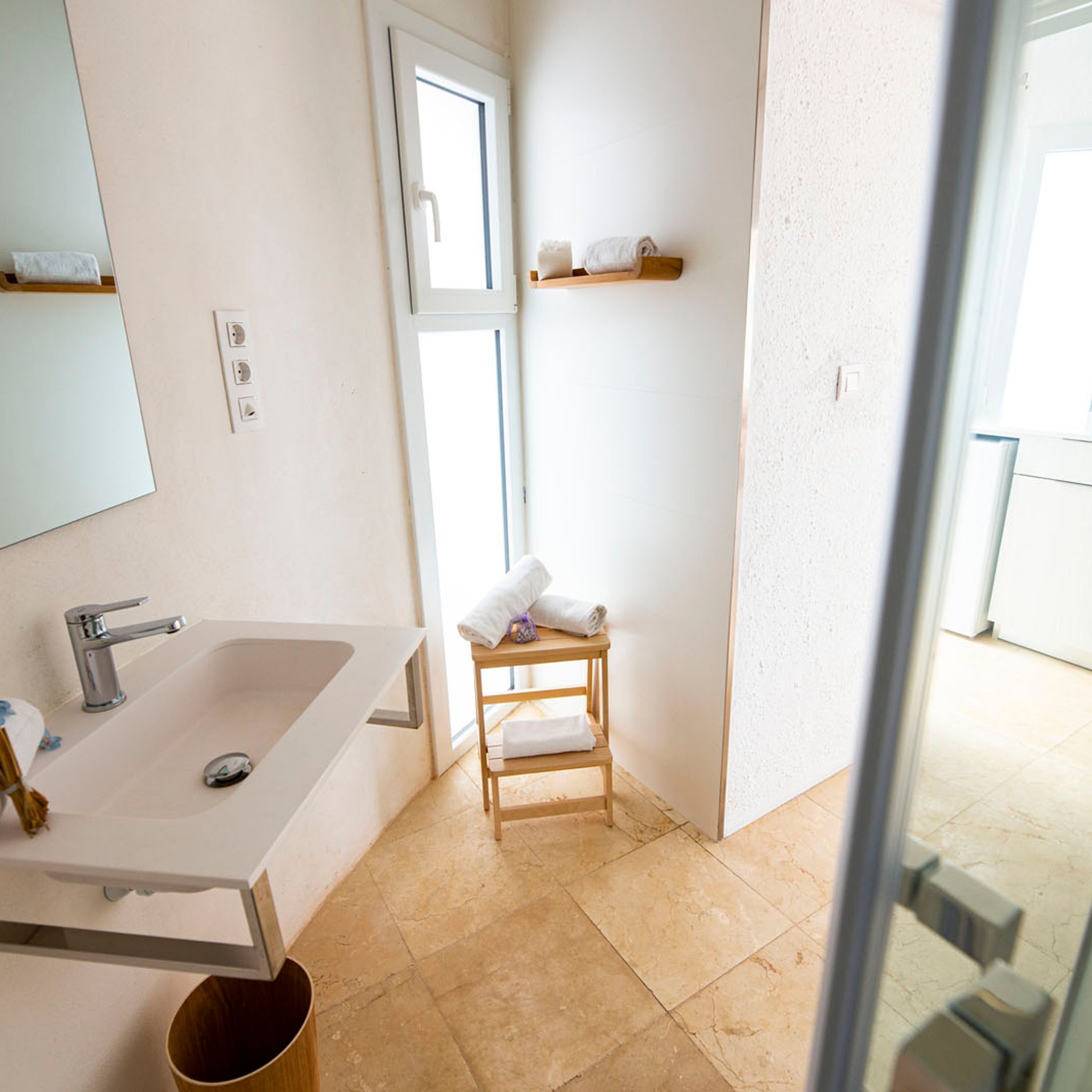 A modern bathroom with a large sink, a mirror, and a wooden stool with towels.