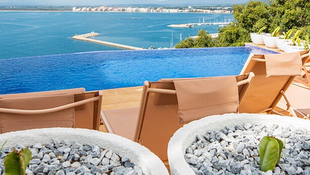 Uma piscina infinita com vista para o mar e uma paisagem urbana distante.