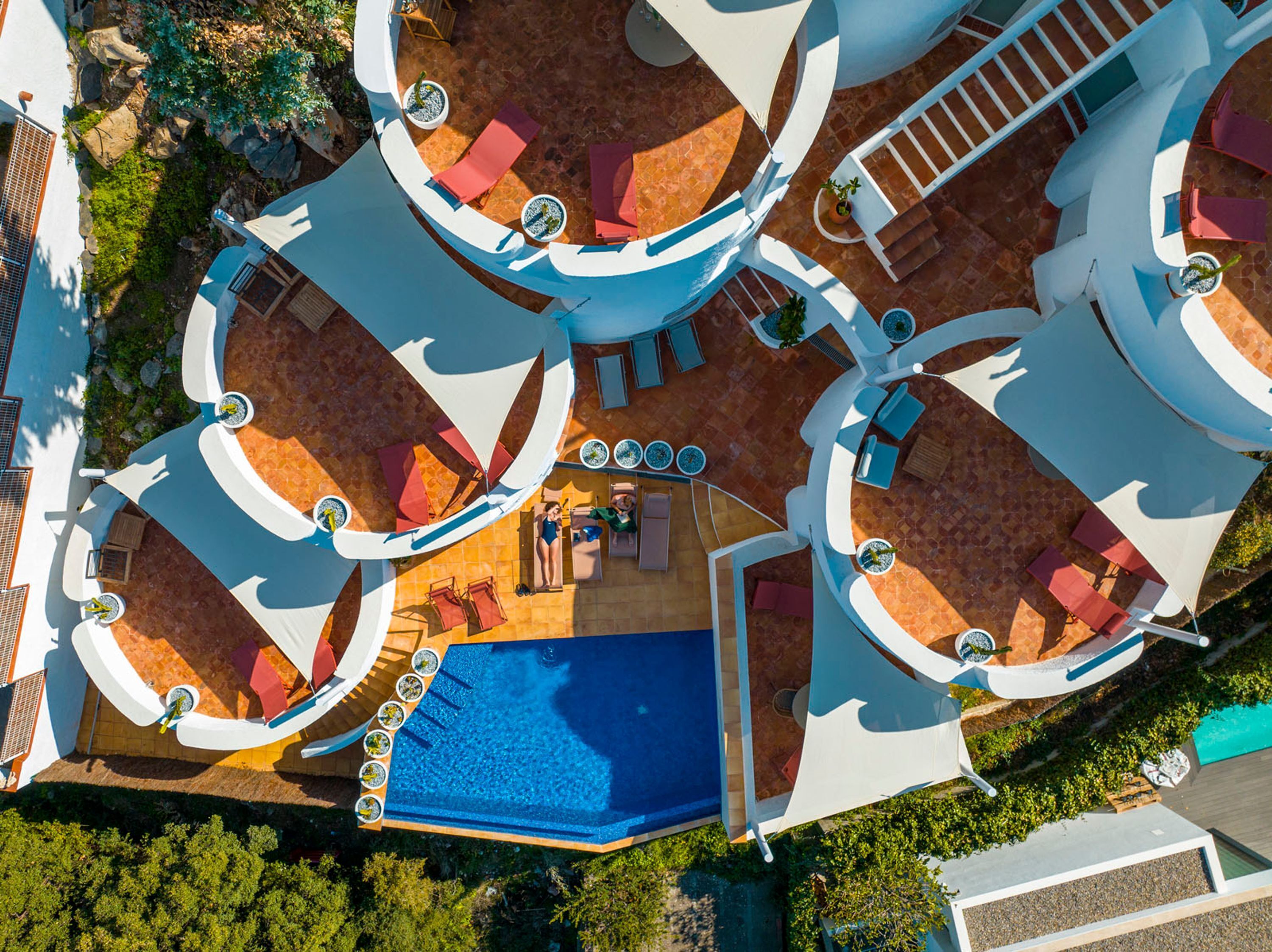 An aerial view of a resort with multiple swimming pools, sun loungers, and a central seating area.