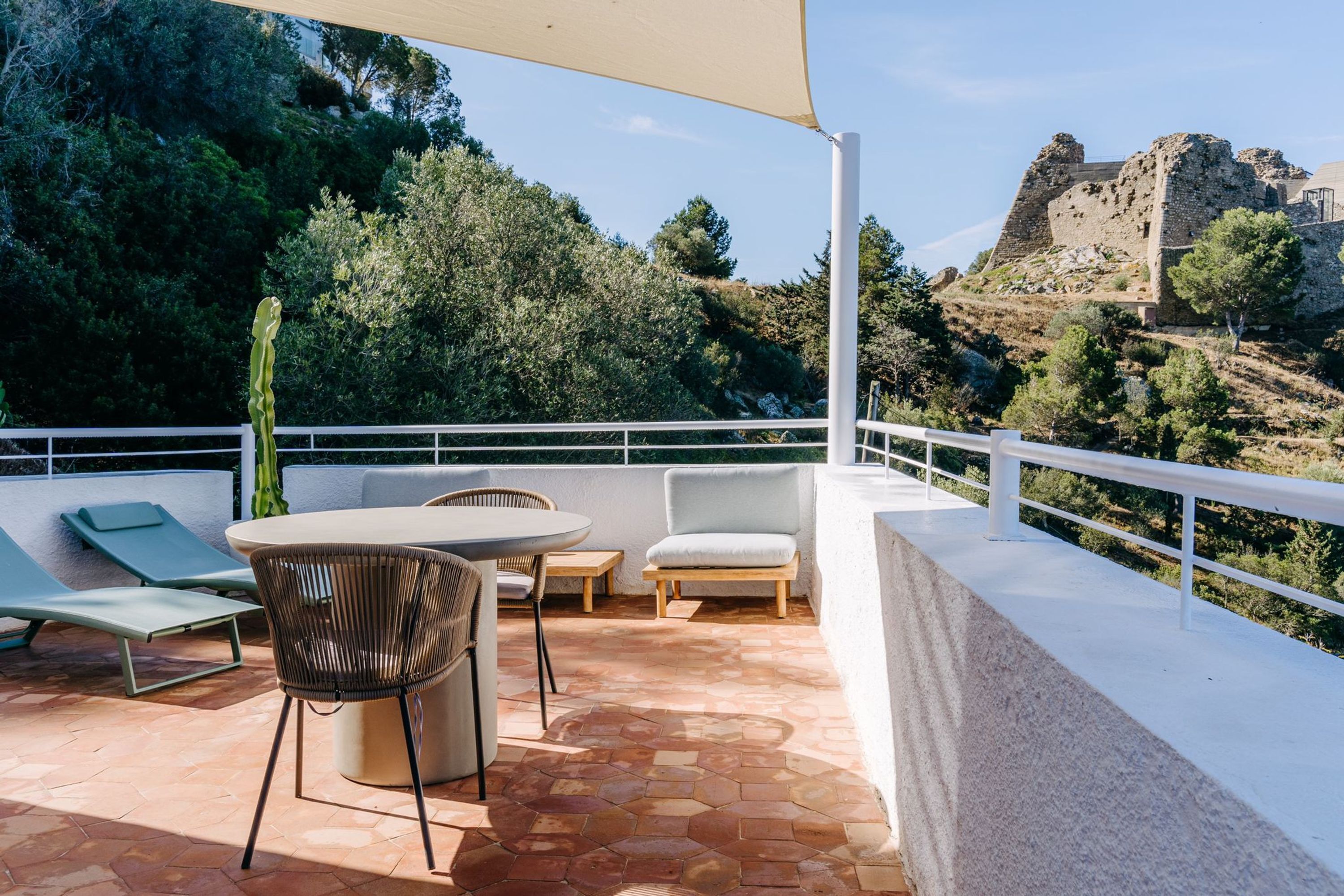 A terrace with a table and chairs, a cactus, and a view of a castle on a hill.