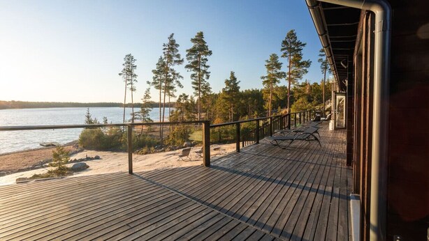 Une terrasse en bois dotée d’une balustrade, qui offre une vue sur un lac et est entourée d’arbres.