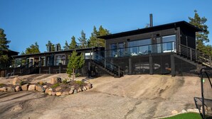 Un bâtiment moderne doté d’une façade en verre, d’un escalier menant à une terrasse et entouré d’un paysage rocheux.