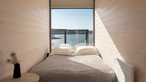 Une chambre avec une grande fenêtre donnant sur une étendue d’eau et sur une côte lointaine.