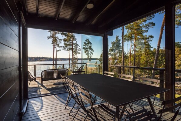 A wooden deck with a table and chairs overlooking a lake and forest.