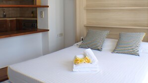 A bedroom with a bed, wooden headboard, and a small kitchenette area. - Porthos 113 in Roses (Roses)