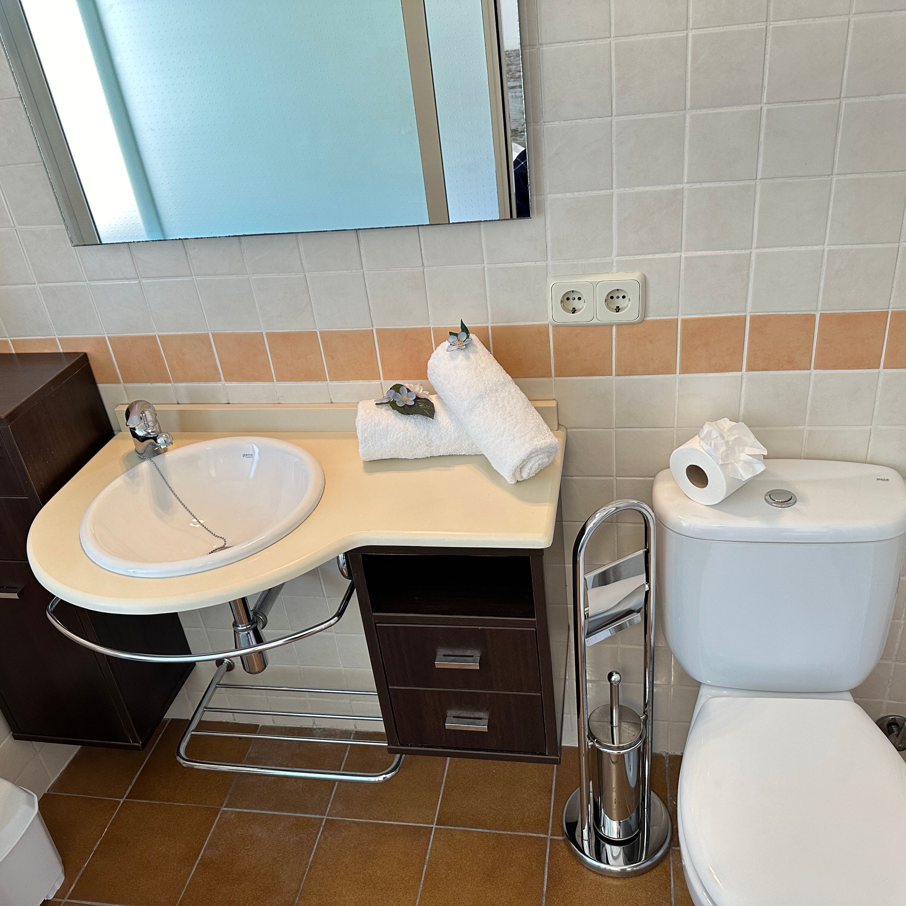 Une salle de bain comprenant un lavabo, un miroir, un porte-serviettes, des toilettes et un petit meuble de rangement.