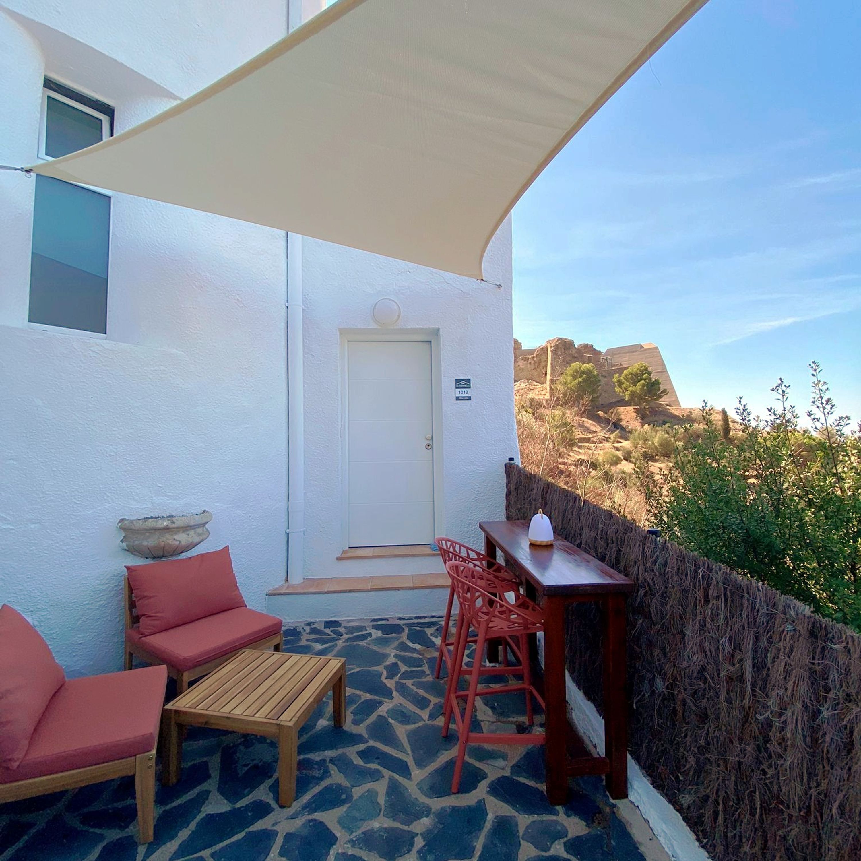 A balcony with a white wall, a door, a table with chairs, and a view of rocky terrain.