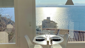 Un comedor con mesa y sillas, vista al mar y un edificio al fondo.