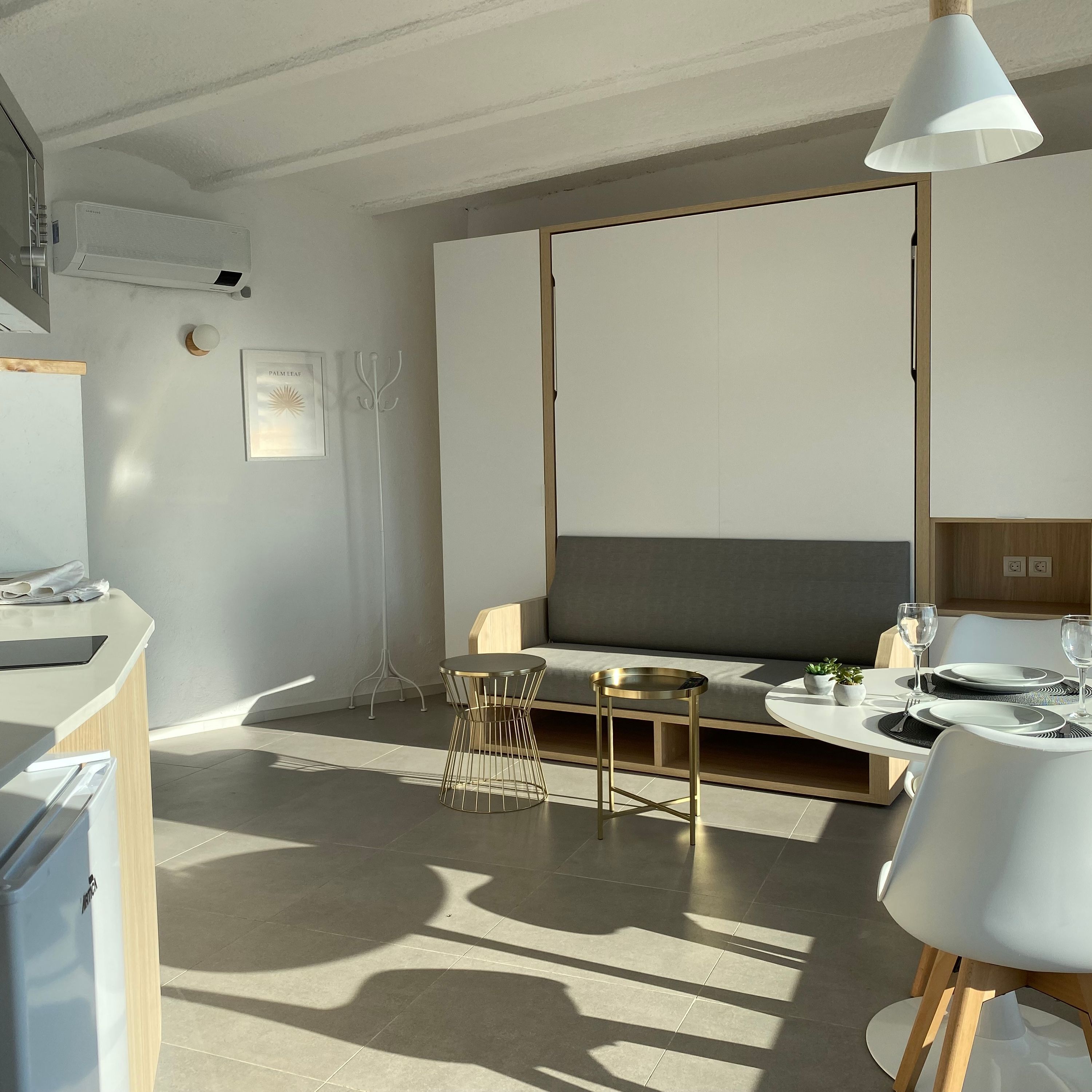 A modern, minimalist room with a sofa, a dining table set for two, and a pendant light.