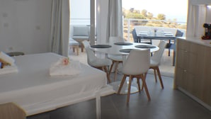 A hotel room with a bed, a dining table with chairs, a balcony with a table and chairs, and a view of the sea.