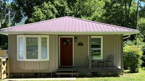A small, single-story house with a red door, a front porch with two chairs, and a metal roof. - NEW Bungalow - Fenced yard - 30+ day rental - View of Lookout Mountain - Chattanooga (Chattanooga)
