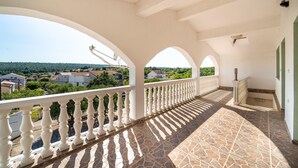 Uma varanda com grades brancas, soalho em azulejos e vista para uma área residencial.