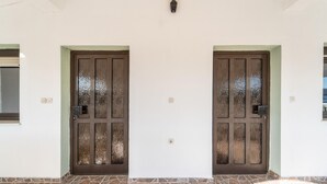 Fachada de edifício com duas portas marrons simétricas, acesso em pedra e uma pequena janela à esquerda.