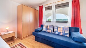 Um quarto com sofá azul, guarda-roupa de madeira e janela com cortinas vermelhas.