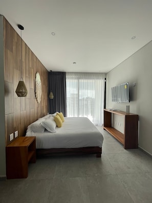 Relax in a serene space with a large bed, flat-screen TV, and natural light pouring in through sheer curtains.